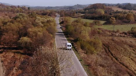 White-Van-Driving-On-Long-And-Winding-Country-Road-In-Autumn---aerial