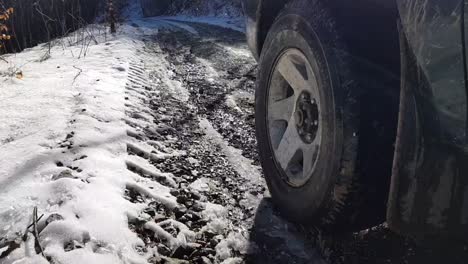 Left-Front-Wheel-Of-A-4x4-Vehicle-Travelling-On-Snowy-Road-In-The-Mountain-In-Winter,-close-up