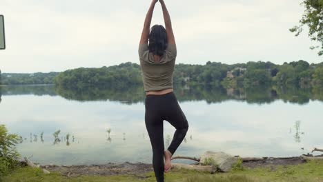 Mujer-Latina-Relajada-Practicando-Yoga-En-Pose-De-árbol-Meditando-En-Roca-Junto-A-Estanque