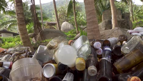 Collected-trash-bottles-piled-up-under-palm-trees-near-the-beach,-steady-shot