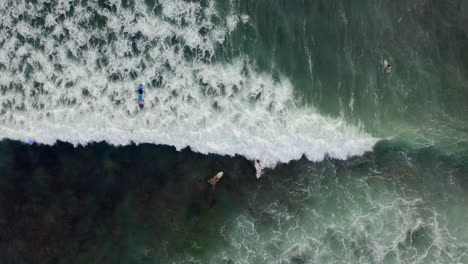 Aerial-view-of-surfers-riding-waves-from-above-blue-ocean