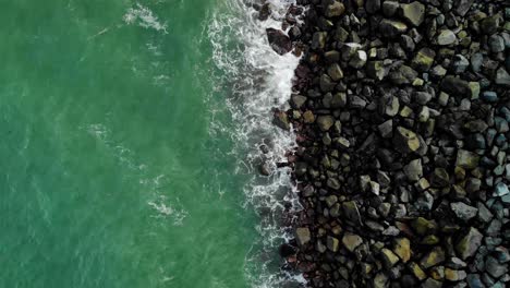 Aerial-view-above-blue-waves-hitting-small-stones---rising,-overhead,-drone-shot