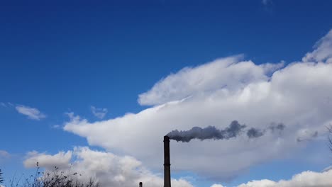 Fabrikschornstein-Gibt-Tagsüber-Dunklen-Rauch-Mit-Blauem-Himmel-Und-Wolken-Im-Hintergrund-Ab