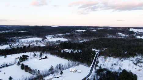 Rural-Upstate-New-York-in-light-snow-at-dusk-in-winter,-drone-aerial-shot-slowly-flies-over-farm-land