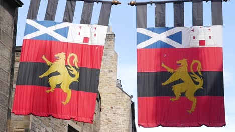 Toma-En-Cámara-Lenta-De-Dos-Banderas-Medievales-De-Dragones-Coloridos-Que-Cuelgan-En-El-Casco-Antiguo-Castillo-De-Escocia-Edimburgo-Reino-Unido-1920x1080-Hd