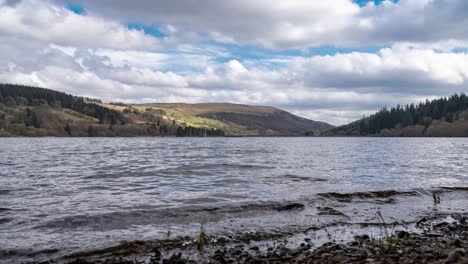 4K-Timelapse-on-waters-edge-as-clouds-roll-across-sky-and-over-hills-at-Llwyn-on-Reservoir,-Brecon-Beacons,-South-Wales-UK