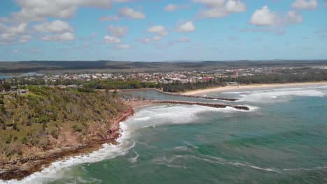 Aerial-drone-view-over-waves-hitting-the-shore-of-the-Evans-Head-town,-sunny-day