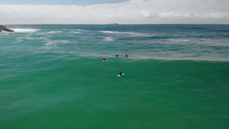 Aerial-drone-view-of-a-surfers-waiting-for-waves,-in-clear-waters-of-the-Emerald-beach,-sunny-day,-in-Australia
