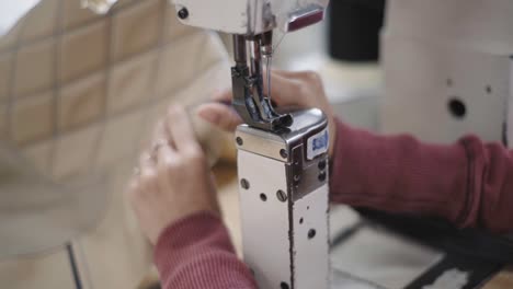 Closeup-of-a-skilled-workers-hands-passing-fabric-through-a-sewing-machine,-inside-workshop