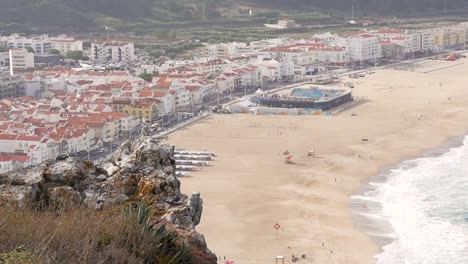 Slow-motion-still-shot-of-Nazare-town-suburb-with-sandy-beach-shops-and-houses-from-cliff-in-Portugal-Europe-1920x1080-HD