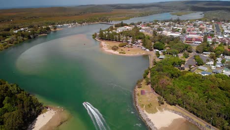 Aerial-view-of-a-boat-on-a-river-and-the-Evans-Head-town,-New-South-Wales,-Australia---tilt-up,-drone-shot