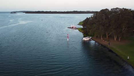 Pelican-bird-flying-with-pan-of-the-lake-The-Entrance-channel-with-town-with-park-Central-Coast-NSW-Australia-3840x2160-4K