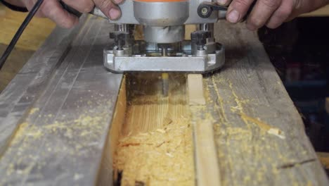 Close-Up-Of-Carpenters-Hands-Working-On-Piece-Of-Wood-With-Router-Machine-On-Workbench