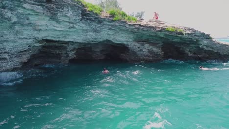 Bermuda-drone-shot-of-divers-swimming-back-towards-caves-under-a-cliff-edge