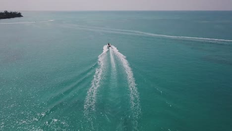 Bermuda-rising-drone-shot-of-a-motor-boat-sailing-out-towards-the-open-ocean-with-jet-skis-in-the-distance
