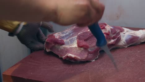 The-butcher-cuts-the-meat-from-the-pig's-leg-with-knife