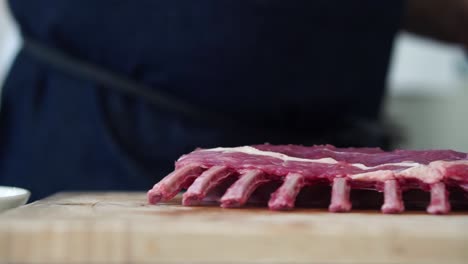 Chef-trimming-the-fat-off-rack-of-lamb-on-chopping-board