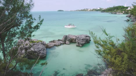 Bermuda-near-Morgan's-Island,-motor-boat-pulling-into-natural-sheltered-cove-with-shallow-turquoise-water-and-tropical-coastline