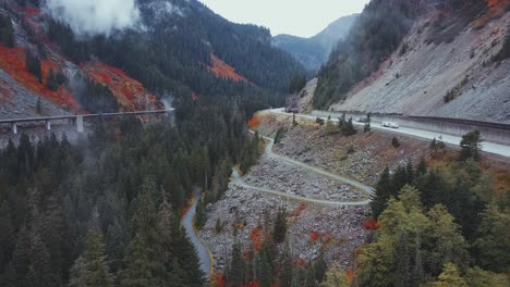 Washington-State---Drone-aerial-rising,-misty-pine-forest-and-mountains-with-a-highway,-trucks,-and-cars,-and-red-fall-colours-near-Franklin-Falls-and-Snowqualmie