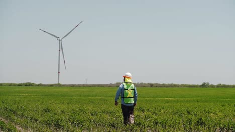Worker-walking-in-a-field-in-front-of-wind-turbines-from-a-wind-farm,-Mexico