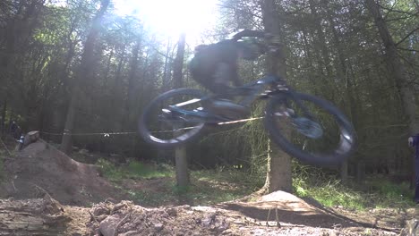 Slow-Motion,-Group-of-Mountain-Bikers-riding-downhill-at-high-speed-in-forestry-track,-taking-large-dirt-jump