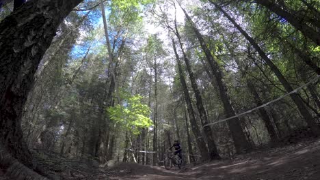 Mountain-Biker-riding-downhill-at-high-speed-in-forestry-track,-curving-around-corner-berms