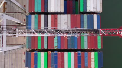 Top-down-aerial-drone-shot-flying-over-container-ship-tilts-up-to-reaval-in-port-unloading-containers