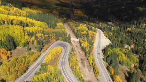 An-aerial-view-of-a-winding-Colorado-road-twisting-down-a-valley-through-mountains-and-changing-aspen-trees-in-the-autumn