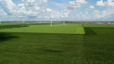 Wide-angle-drone-aerial-footage-zoom-into-wind-turbines-spinning-on-a-clear-summer-day-over-a-green-field-in-Texas