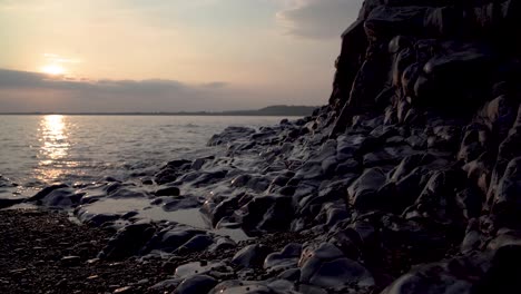 Tides-washing-over-pebble-beach-at-the-foot-of-rocks-at-sundown,-Ogmore-on-Sea,-South-Wales,-UK