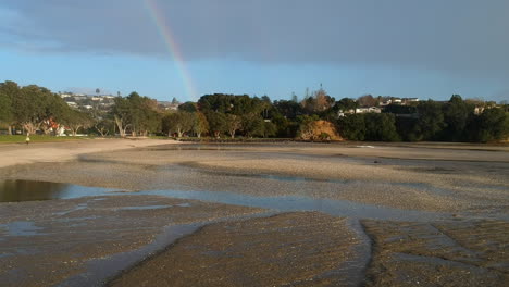 Drone-flying-forward-on-a-beach-through-rain-towards-a-rainbow-at-the-end-of-the-beach