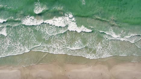 Aquamarine-waves-crash-against-warm-golden-sand-from-a-bird's-eye-view-in-a-drone-in-slow-motion