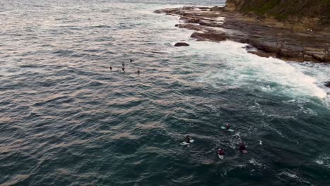Drone-aerial-shot-of-coastline-the-Haven-headland-Terrigal-with-Surfers-waiting-in-ocean-Central-Coast-NSW-Australia-4K
