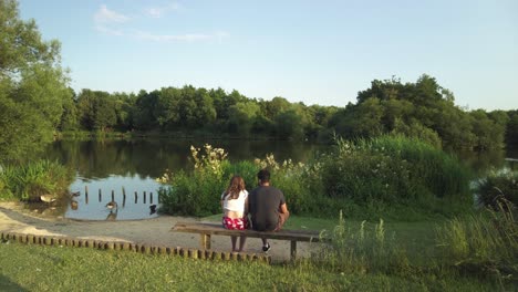 A-couple-sitting-on-a-bench-in-front-of-a-lake-with-geese-during-sunset