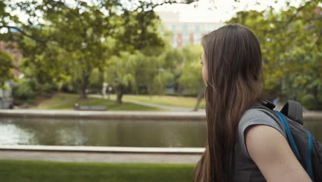 Female-Student-Casually-And-Curiously-Walking-Through-Campus-Exploring-Near-Water,-Side-Profile-Shot