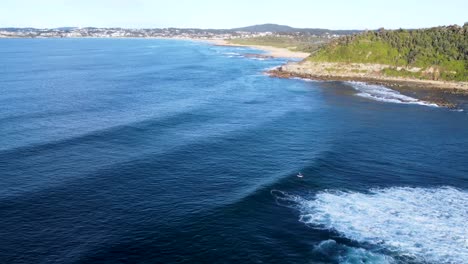 Drone-aerial-landscape-shot-of-headland-and-kayaker-in-morning-waves-at-Forresters-Beach-Central-Coast-Pacific-Ocean-NSW-Australia-4K