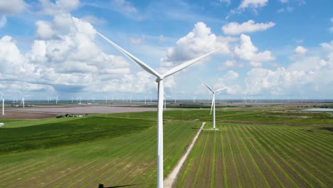 Rotating-Panning-shot-of-Wind-Turbines-spinning-over-a-green-field-on-a-summer-day-with-clouds