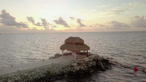 AERIAL---A-cabana-in-rocky-pier-at-sunrise,-Cancun,-Mexico,-wide-spinning-shot