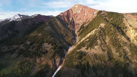 A-colorful-crowning-mountain-peak-with-a-snow-melt-waterfall-running-down-middle-is-seen-on-a-bright-blue-sky-day-located-in-Colorado-near-Crested-Butte