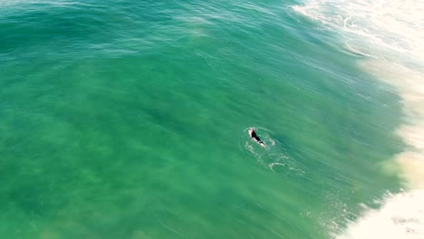 Drone-aerial-view-of-wave-breaking-whilst-surfer-is-paddling-out-off-sandy-beach-break-The-Entrance-Pacific-Ocean-NSW-Central-Coast-Australia-4K