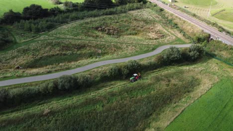 Tractor-in-field-driving-near-hedge-and-bush,-aerial-view-above,-far
