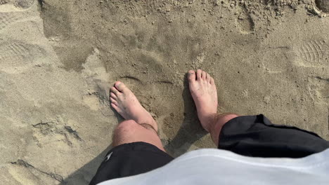 Looking-down-at-legs-and-feet-without-shoes-of-a-male-person-standing-on-a-beach