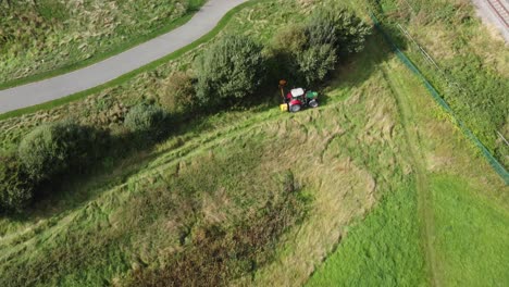 Tractor-in-field-trimming-overgrown-hedge-and-bush,-aerial-view-overhead