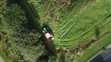 Tractor-in-field-trimming-overgrown-hedge,-aerial-view-tracking-tractor