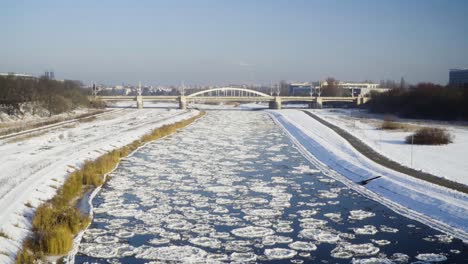 Frozen-river-with-ice-floes-with-a-bridge-and-the-city-in-the-background