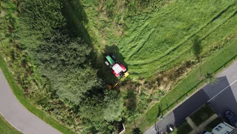 Tractor-in-field-trimming-overgrown-hedge-and-bushes,-aerial-pull-up-shot