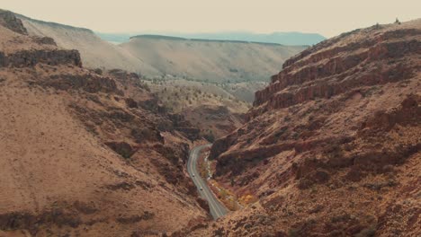 4k-Aerial-red-canyon-with-country-road-in-middle-and-rocky-hill-in-foreground-Drone-dolly-out