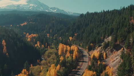 4k-aerial-country-road-in-colorful-forest-in-fall-with-snowy-mountain-in-background-drone-tilt-up