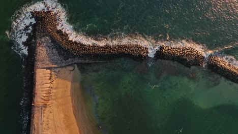 A-birds-eye-view-of-a-breakwater-stopping-waves-at-golden-hour