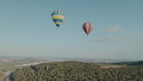 4k-Aerial-two-hot-air-balloons-above-forest-with-city-in-background